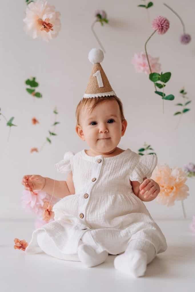 Visual Hook: A charming, soft-lit portrait of a baby in a white dress and a burlap part...