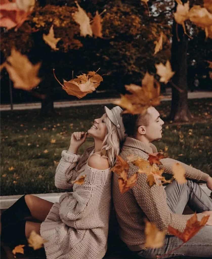 Visual Hook: A couple sits back-to-back on a bench, framed by a cascade of vibrant autu...