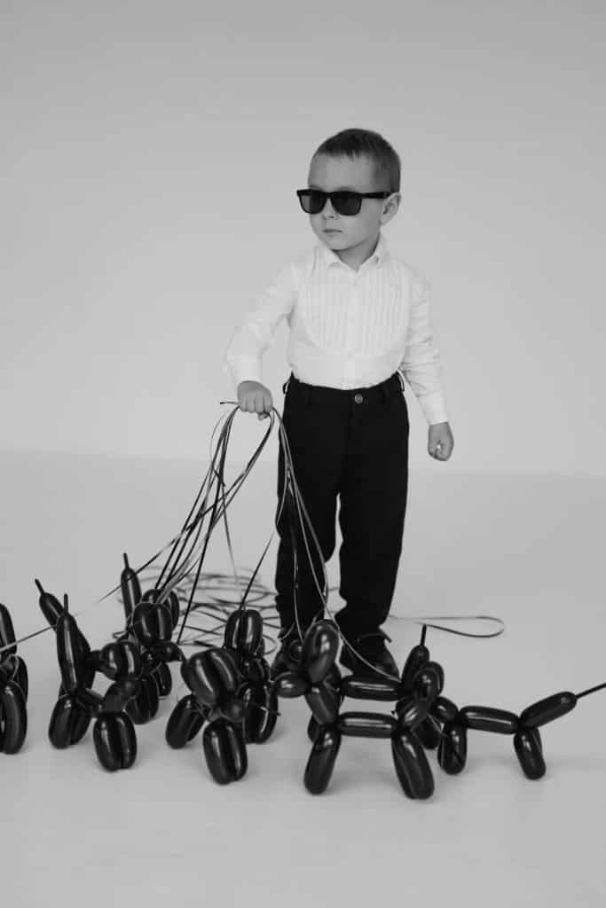 Visual Hook: A stylish child in dark sunglasses leads a pack of shiny balloon dogs on l...