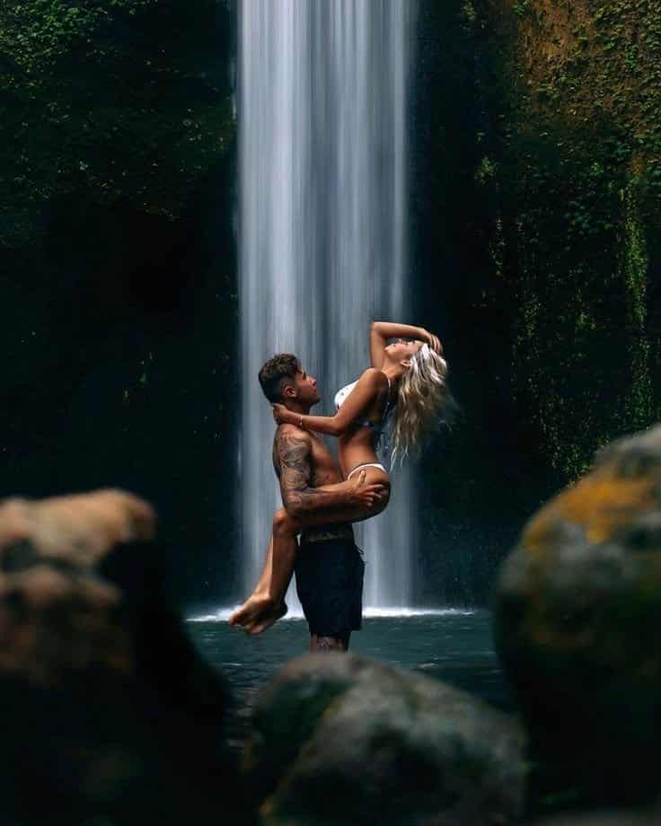 Visual Hook: A romantic embrace under a powerful tropical waterfall, framed by natural...